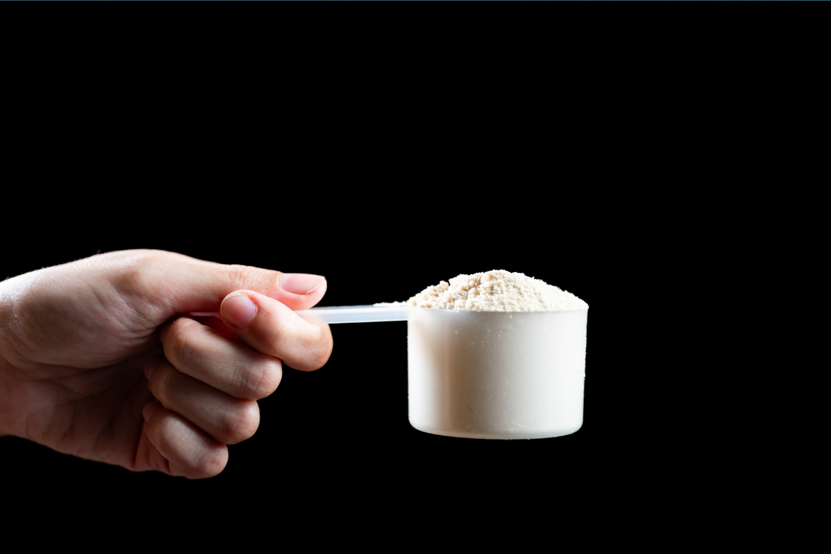 A hand holding a scoop of white powdered supplement against a black background.