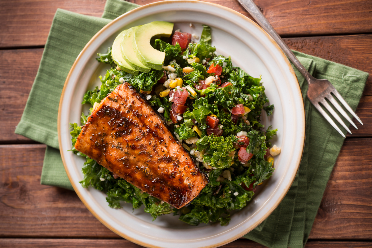 Berry-glazed salmon served on a bed of kale salad with avocado slices, highlighting its nutritious and anti-inflammatory ingredients.