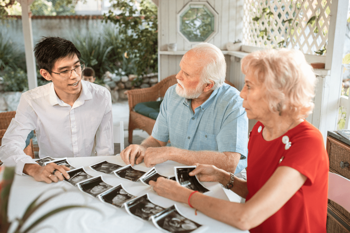 Young man showing ultrasound images to an elderly couple at a table outdoors.