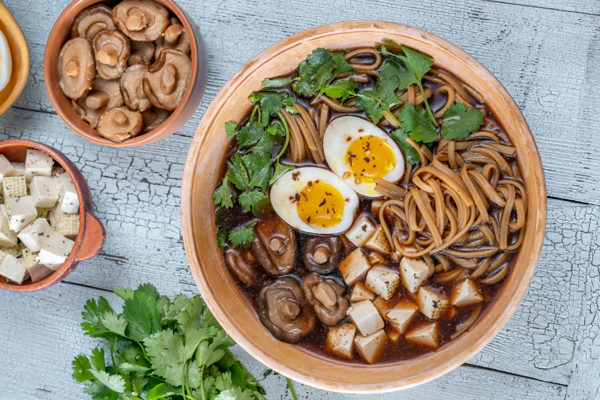 A bowl of miso noodle soup with tofu, featuring noodles, cubed tofu, sliced mushrooms, soft-boiled eggs, and fresh cilantro in a rich broth.