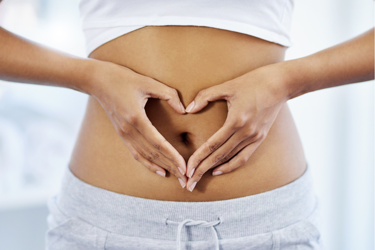 Woman holding hands in heart shape over her tummy, symbolizing good gut health and well-being.