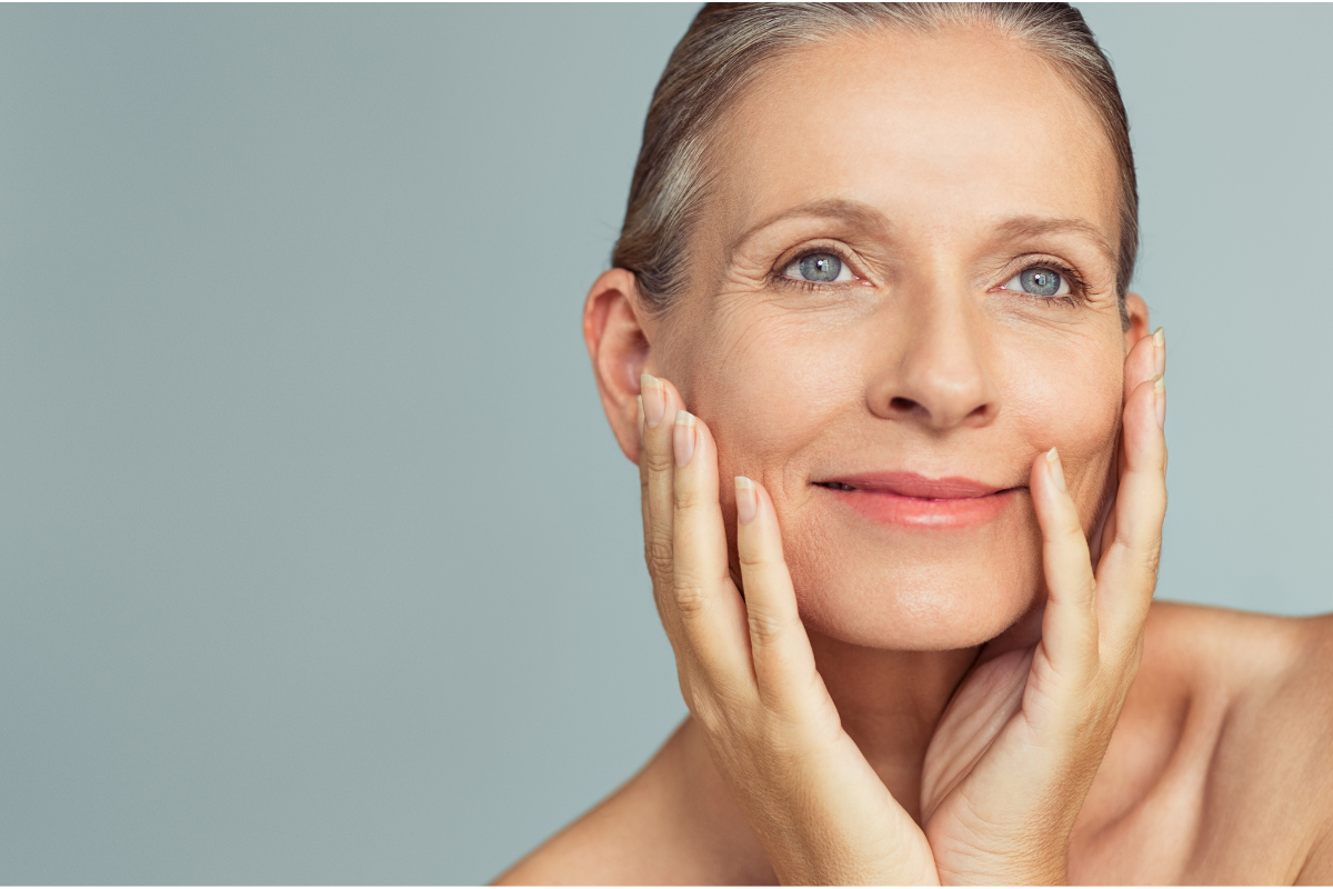 A close-up of a mature woman with smooth, healthy skin, gently touching her face.