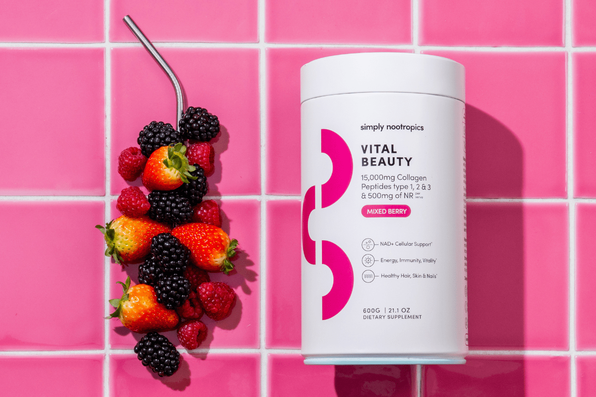 Vital Beauty on a pink tiled background, surrounded by fresh mixed berries.