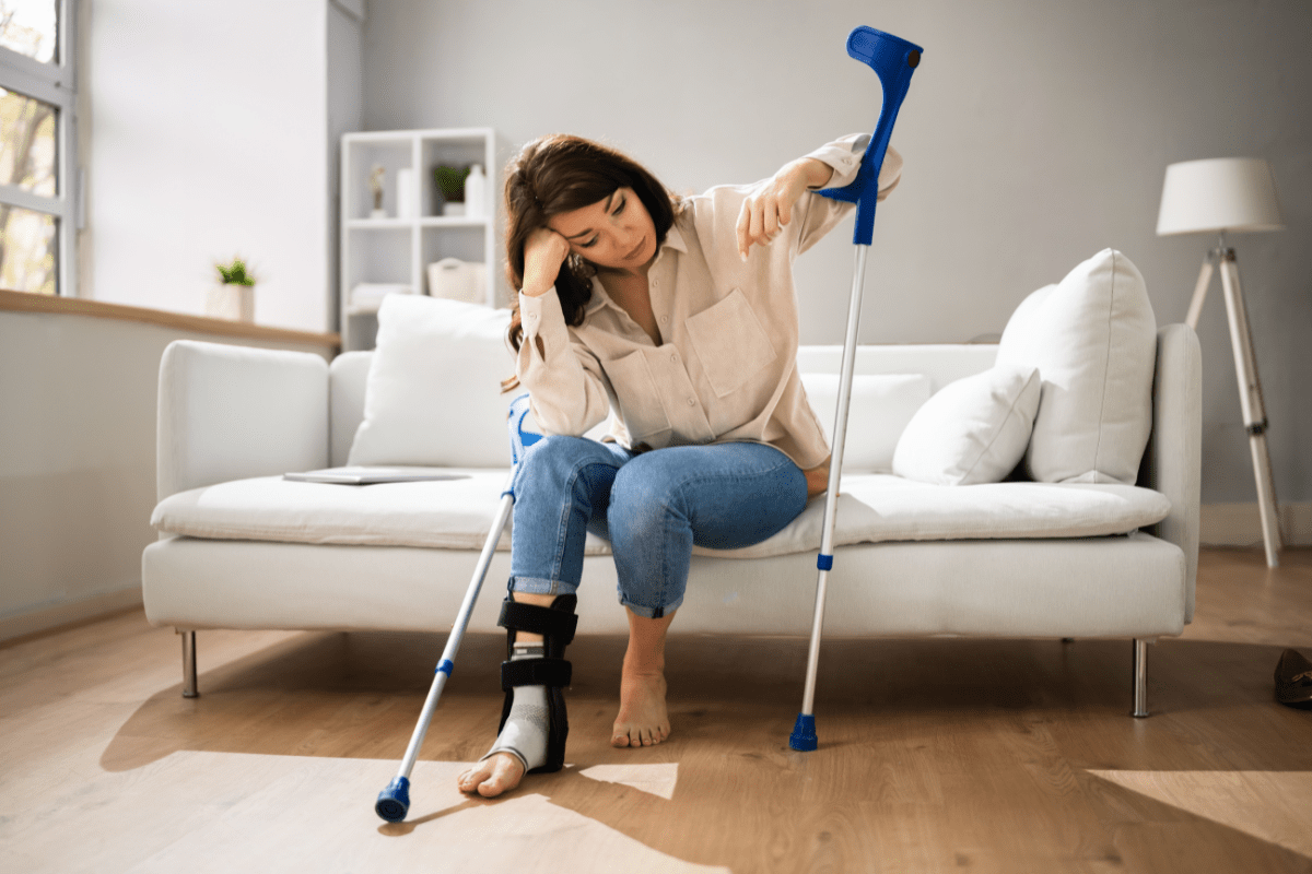 Woman with crutches and a leg brace sitting on a sofa.