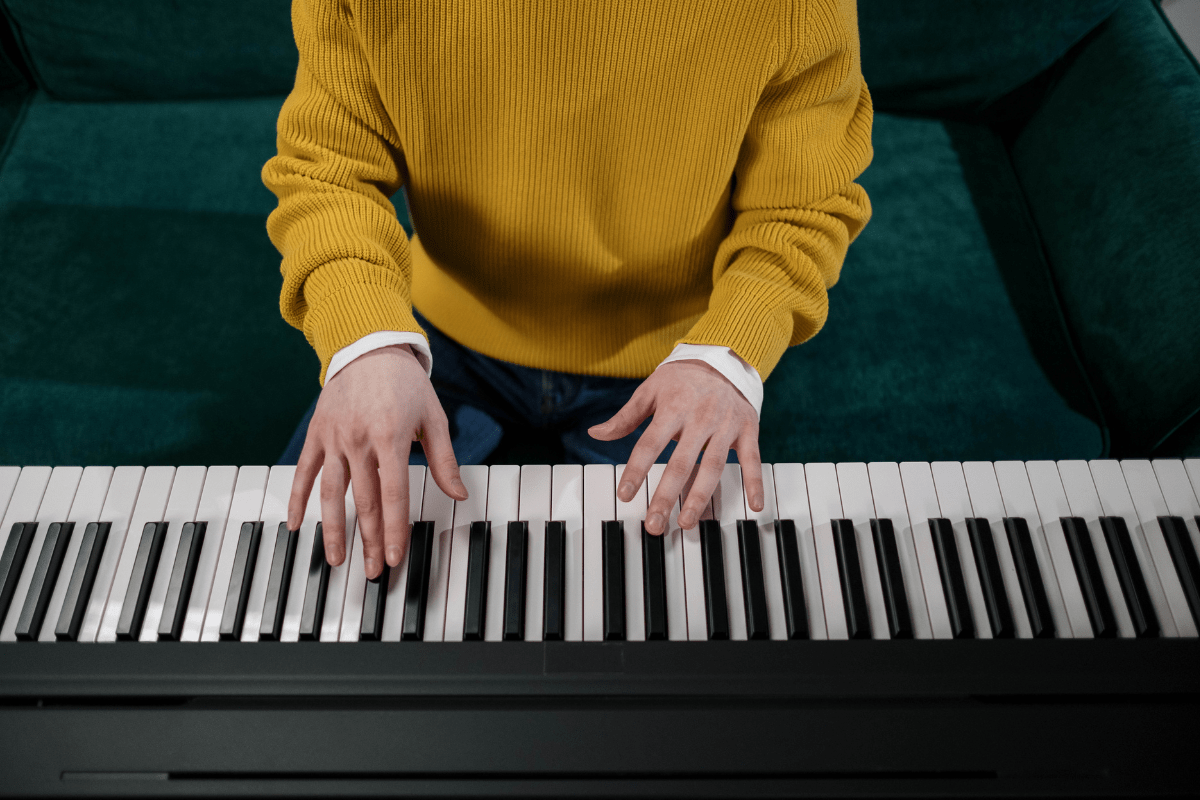 Person in a yellow jumper playing a keyboard piano.
