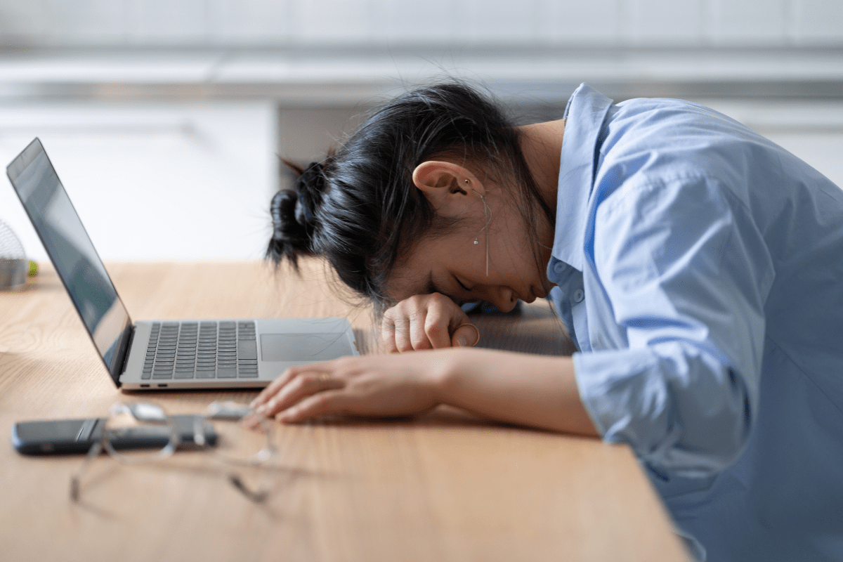 Person with head down on desk in front of a laptop.