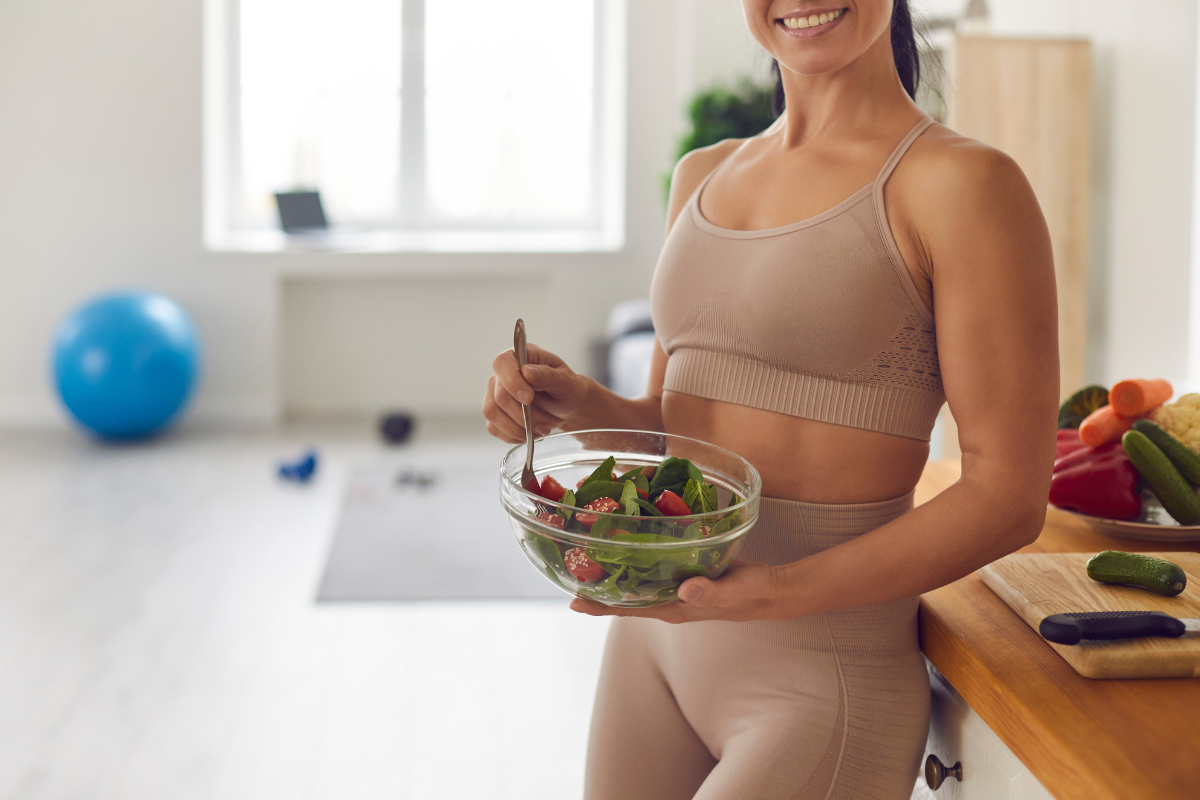 Woman in sportswear holding a fresh salad bowl in a kitchen.