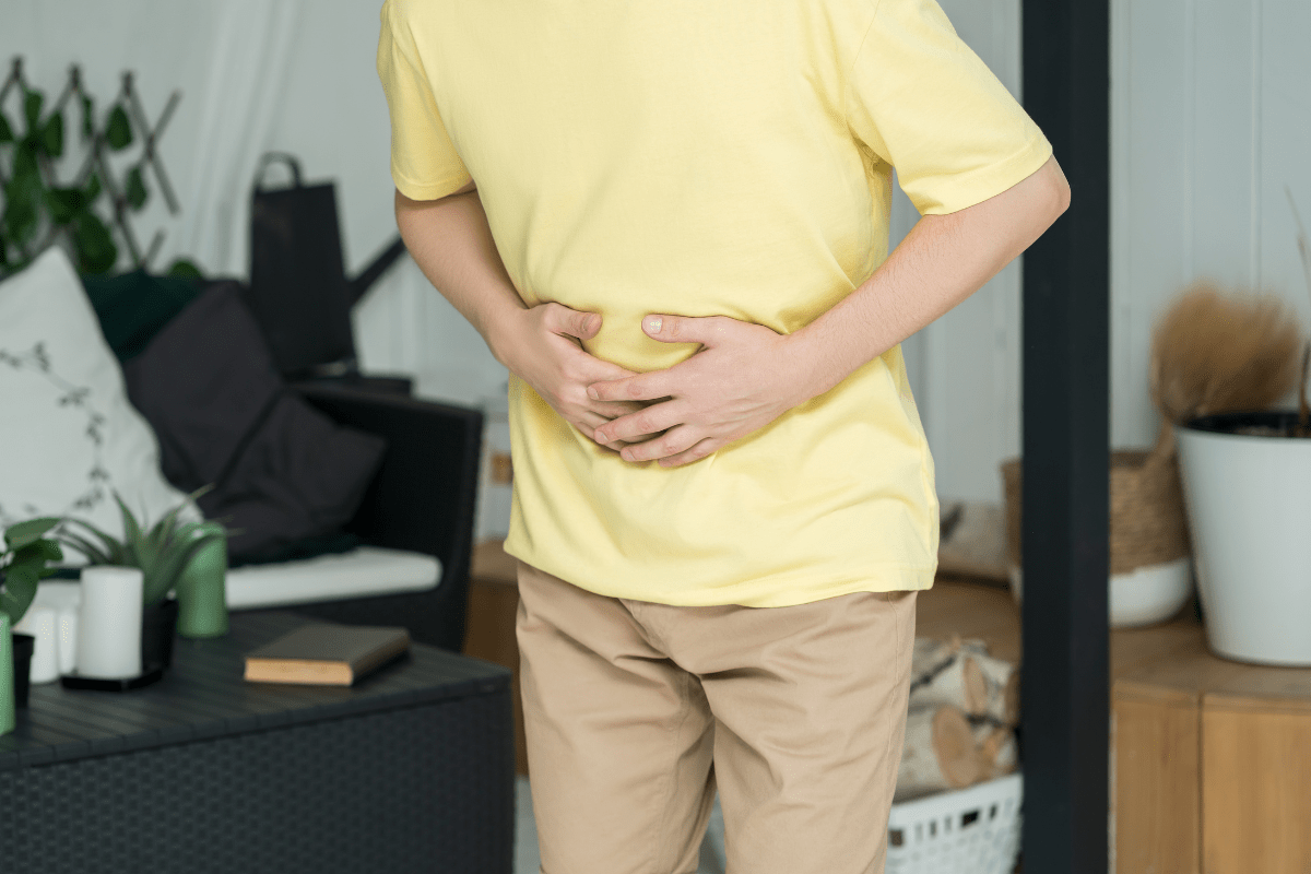 A person in a yellow shirt holding their stomach, appearing to experience discomfort in a home setting.