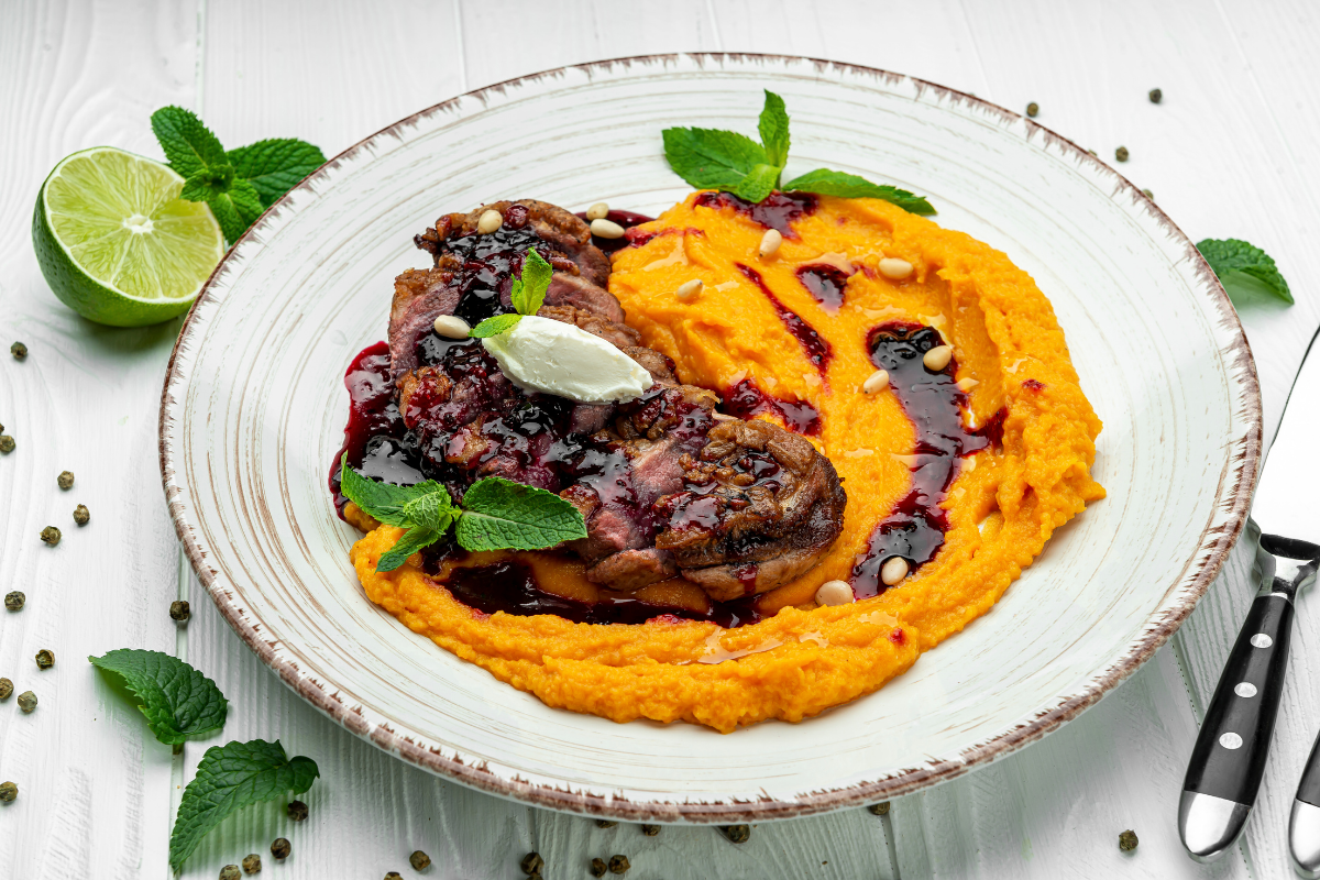 Pan-seared duck breast with berry glaze and sweet potato mash on white plate.