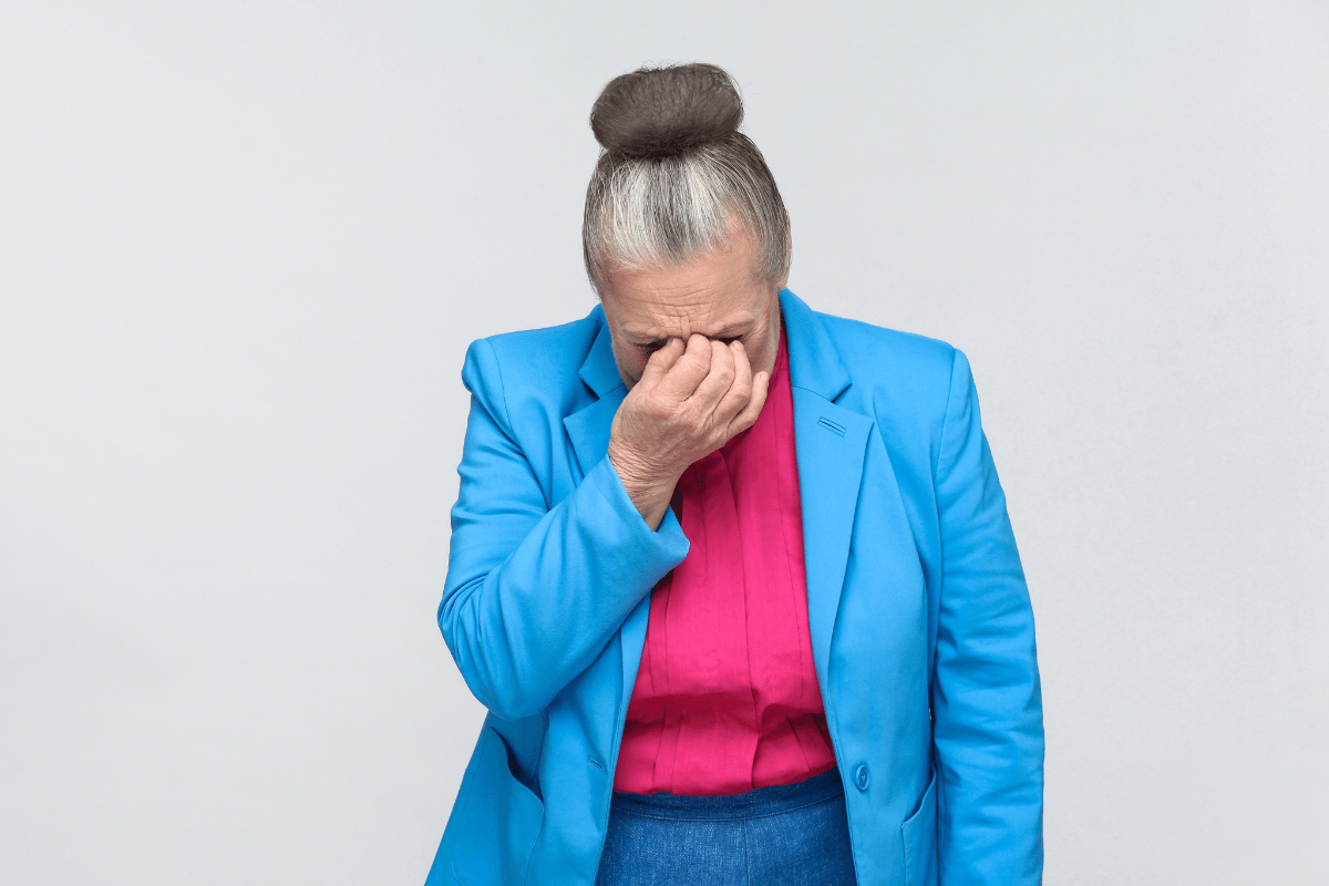 Tired older woman in bright clothes holding her face.