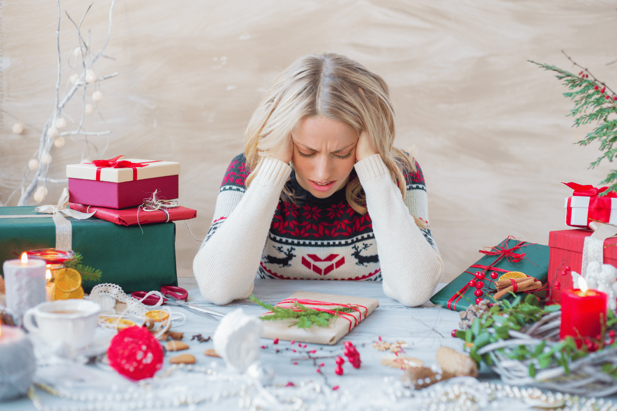 Woman sitting at a table with holiday decorations, holding her head in stress.