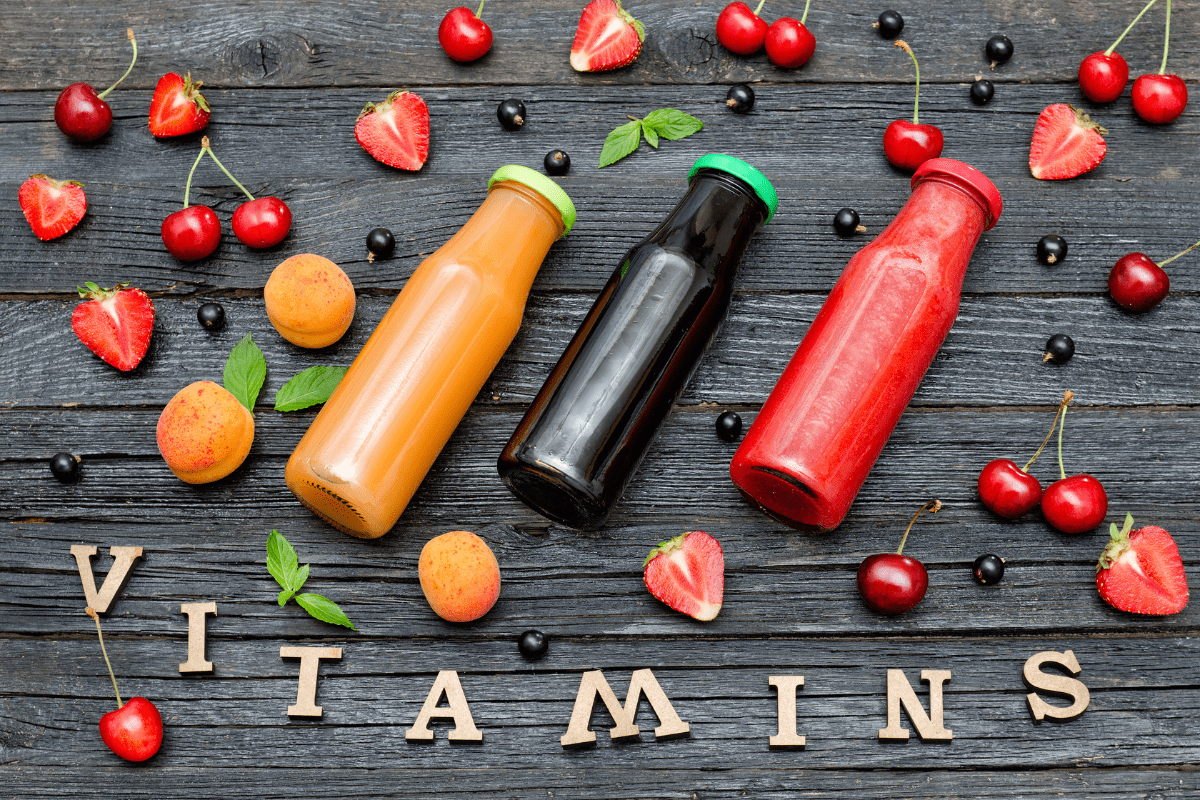 Bottles of fruit juice surrounded by the word “VITAMINS” in wooden letters.