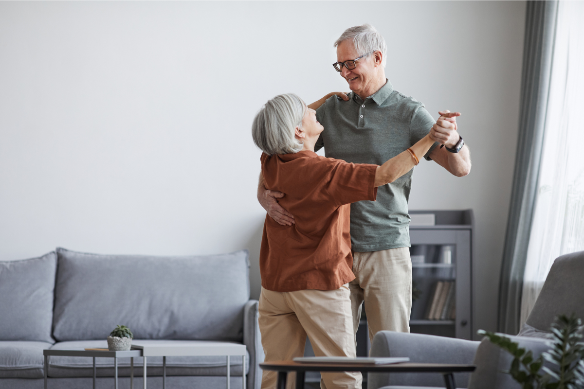 Elderly couple dancing together happily in their living room.