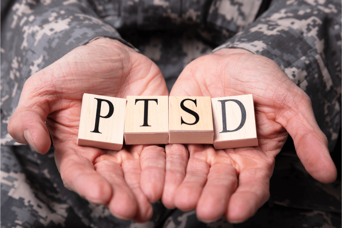 Hands of a person in camouflage uniform holding wooden letter blocks spelling 