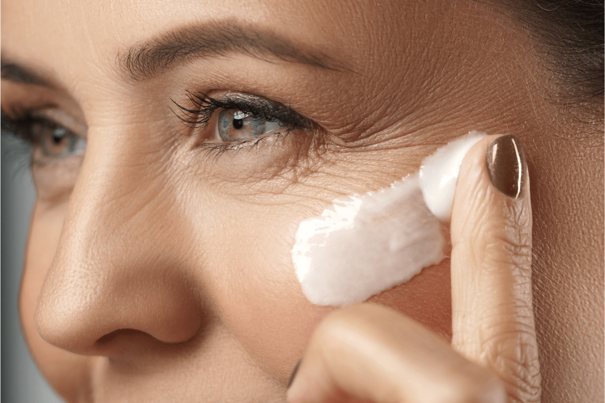 Woman applying cream to the skin around her eye to support ageing skin.