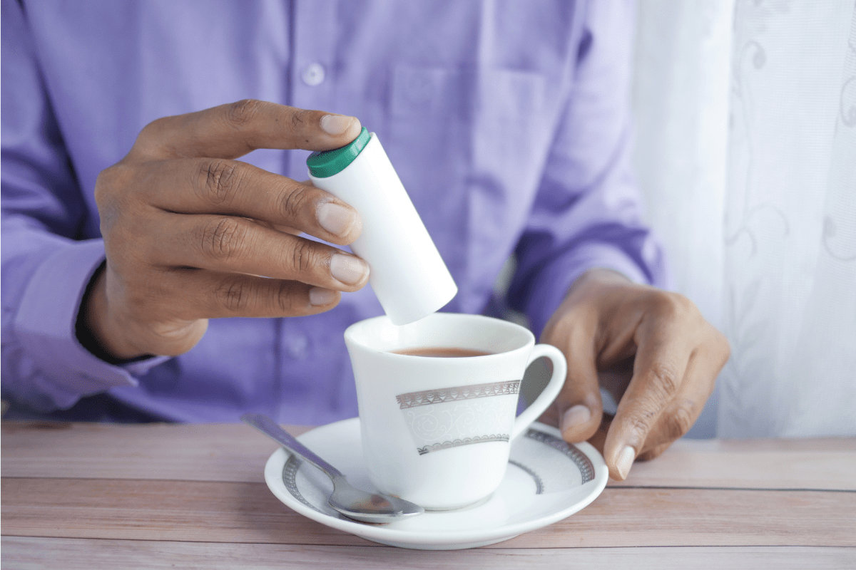 Person adding sweetener to a cup of tea.