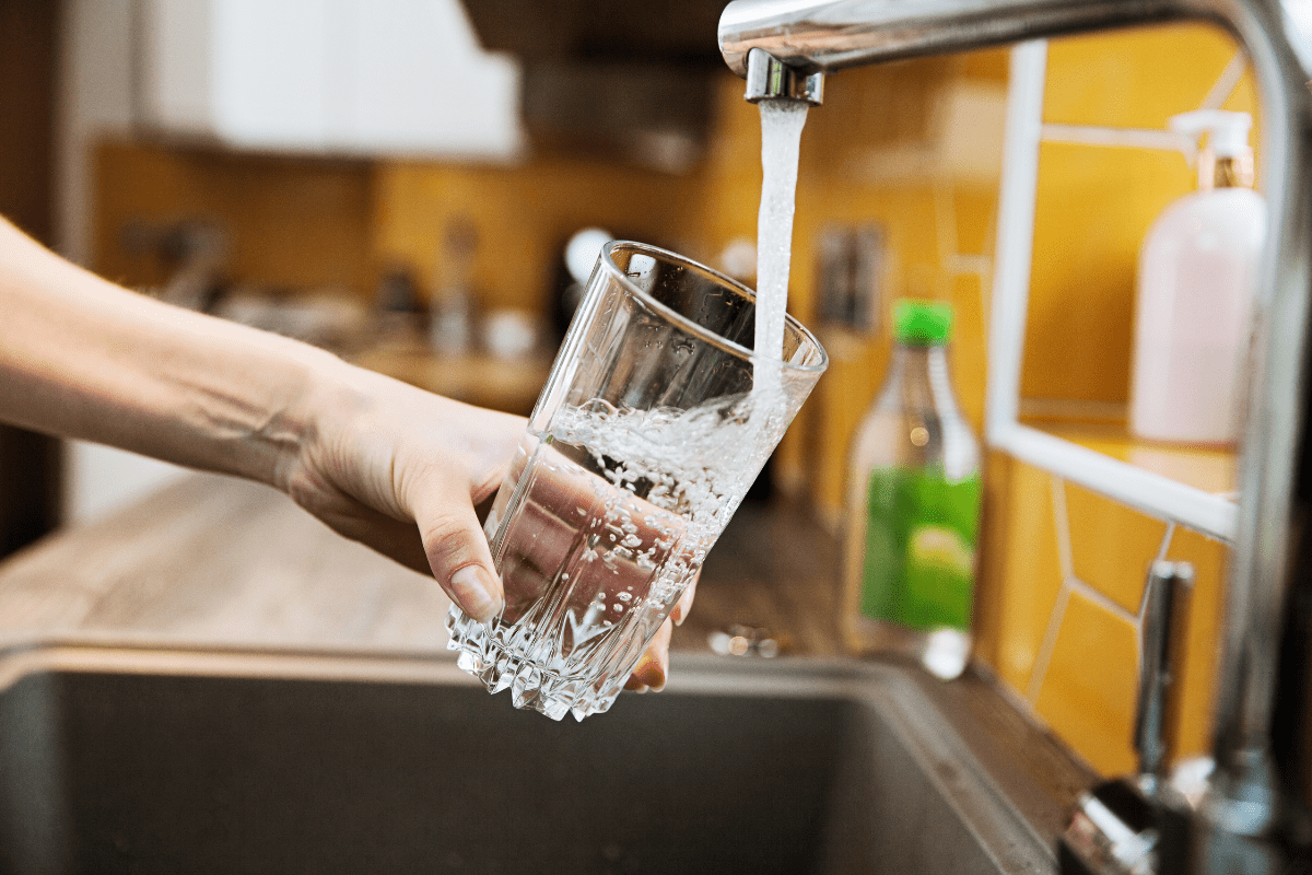 A hand holding a glass under a running kitchen tap, filling it with water.