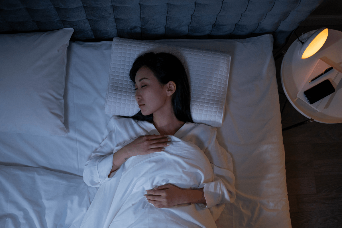 A woman sleeping peacefully on a white bed with a quilted pillow.