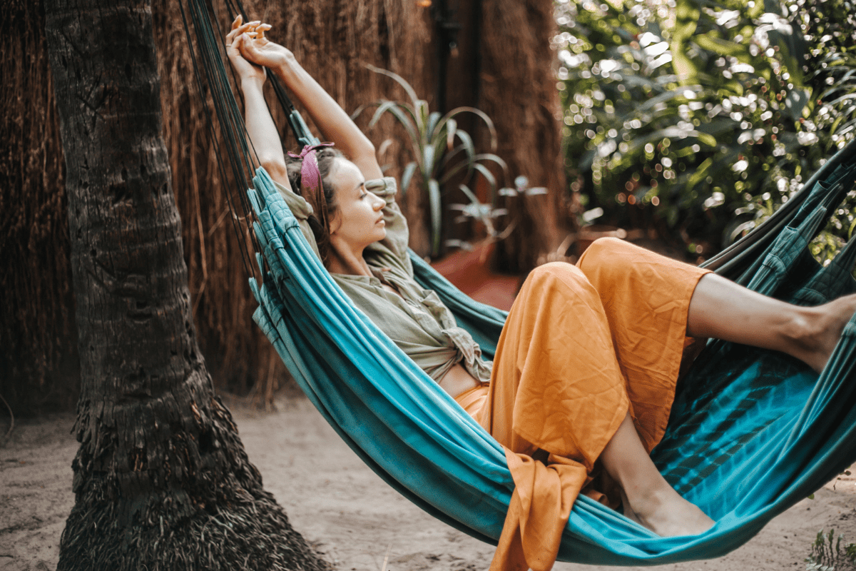 Person relaxing in a blue hammock outdoors surrounded by tropical greenery.