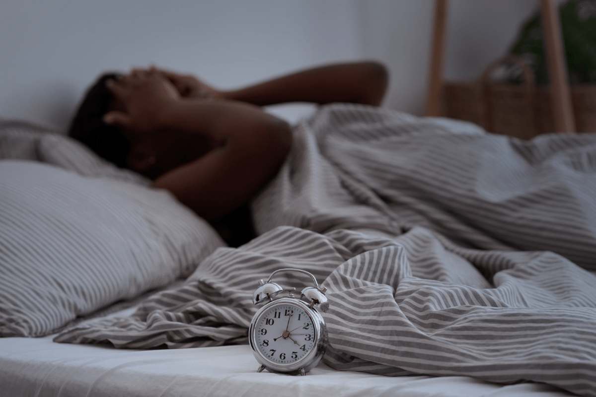 Person lying awake in bed at night while an alarm clock shows 3:55 AM.