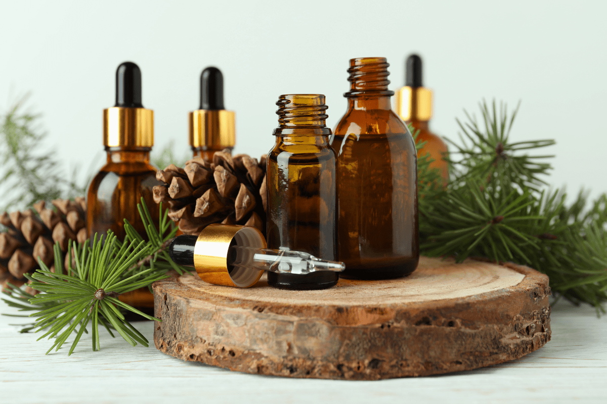 Brown glass dropper bottles on a wooden slab, surrounded by pine branches and pinecones.