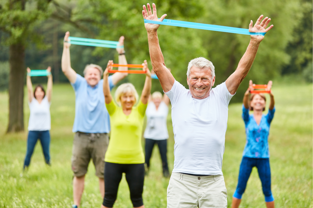 Seniors exercising with resistance bands outdoors, smiling and enjoying physical activity in a park.