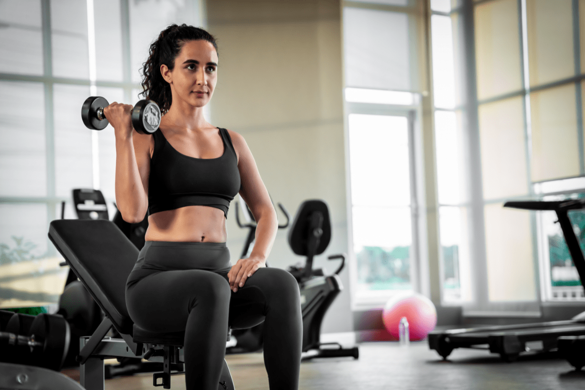 Woman in gym lifting dumbbell while seated.
