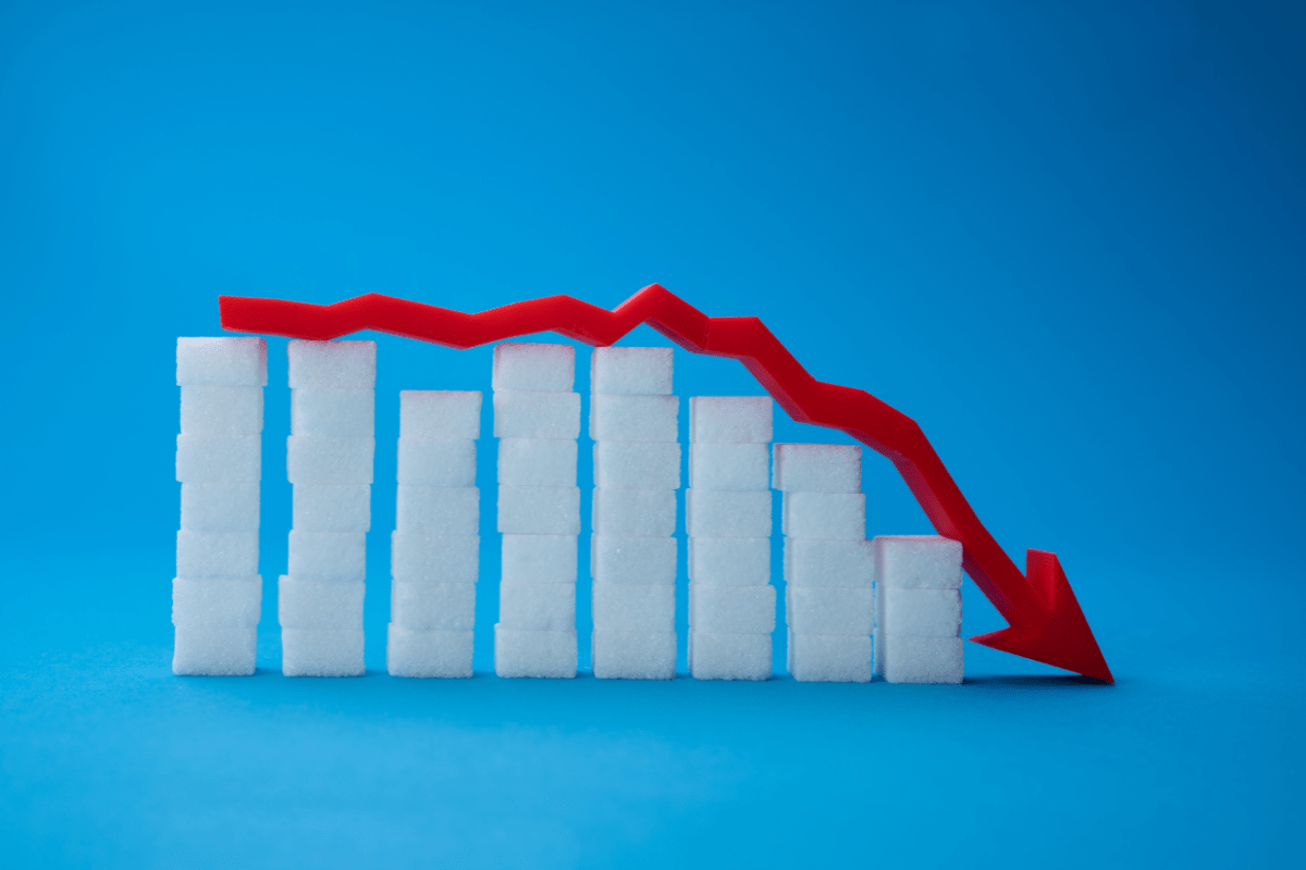 Stacked sugar cubes with a red downward arrow on a blue background, symbolizing reduced sugar levels.