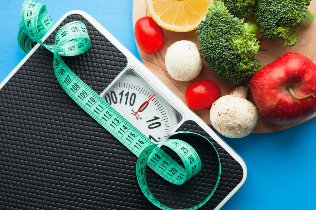 Scale with a measuring tape and fresh fruits and vegetables on a cutting board.