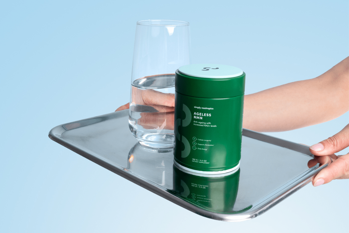 Hand holding a tray with a green container of Simply Nootropics Ageless NMN supplement.