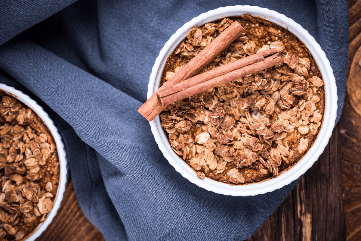 Baked oats with apple and cinnamon sticks in a white ramekin.