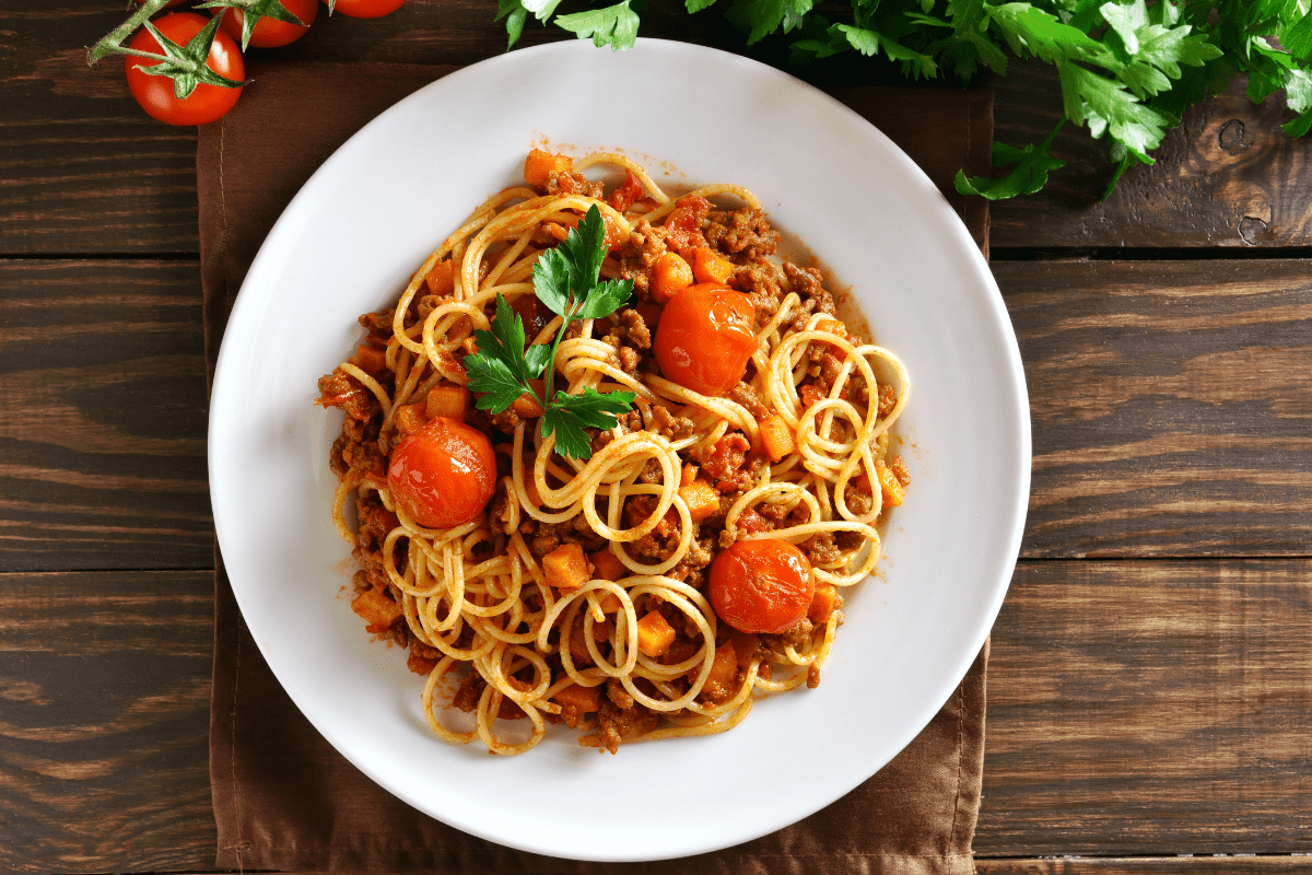 Image of a plate of vegetarian spaghetti Bolognese topped with cherry tomatoes and garnished with parsley on a wooden table.