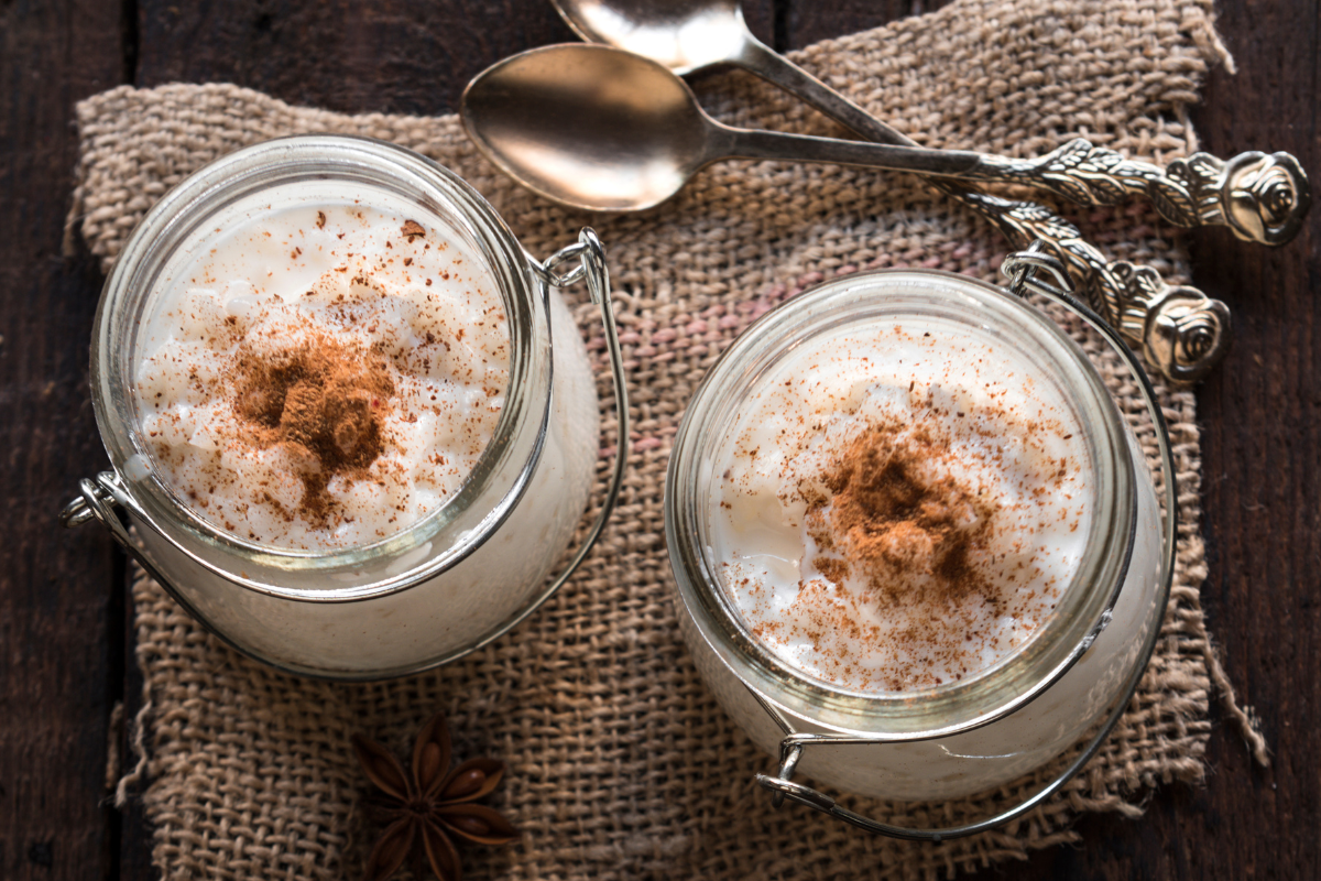 Two jars of coconut rice pudding topped with cinnamon, served on a rustic burlap cloth with spoons beside them.