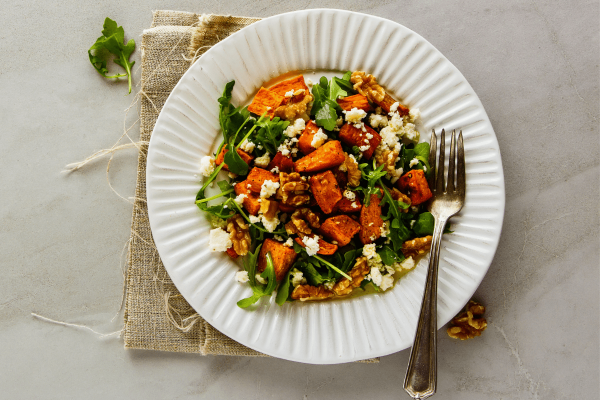 Plate of roasted sweet potato and turkey salad with walnuts, feta, and greens, served on a white dish with a fork.