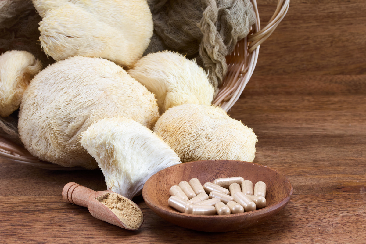 Lion's Mane mushrooms alongside a bowl of capsules and mushroom powder on a wooden surface.