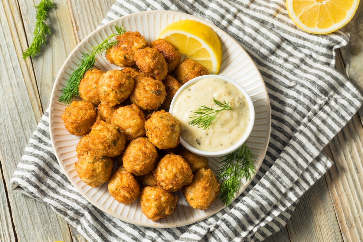 Plate of golden, crispy crab cakes served with a creamy dipping sauce, garnished with fresh dill and lemon wedges.